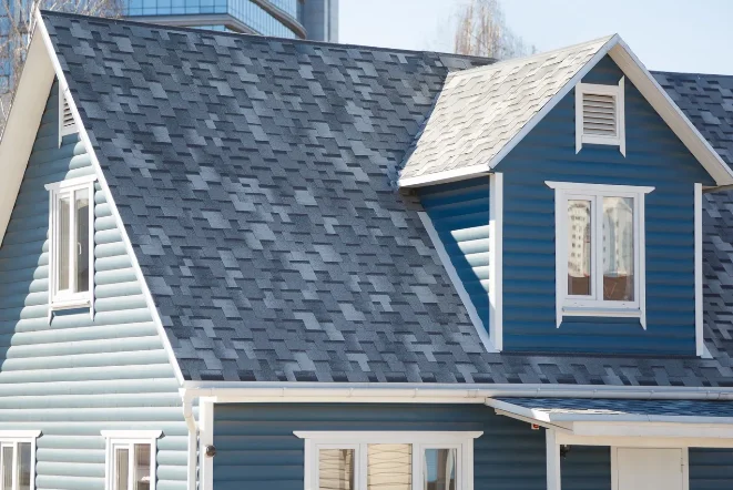 A modern house with blue siding and a multi-toned blue and gray shingle roof, including a prominent dormer
