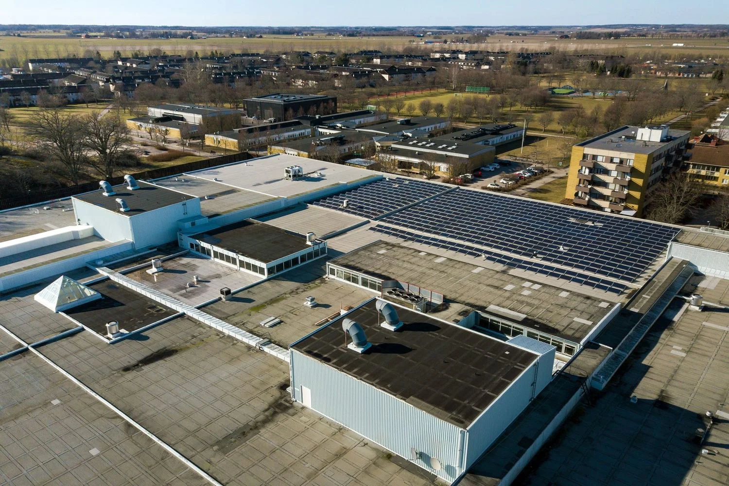 An aerial view displays multiple flat roofs, many extensively covered with solar panels